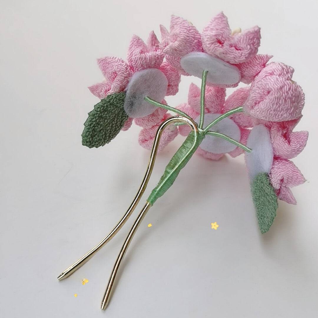 Backside of pink cherry blossom hairpin showing metal prongs and green leaves, part of Japanese headdress set.