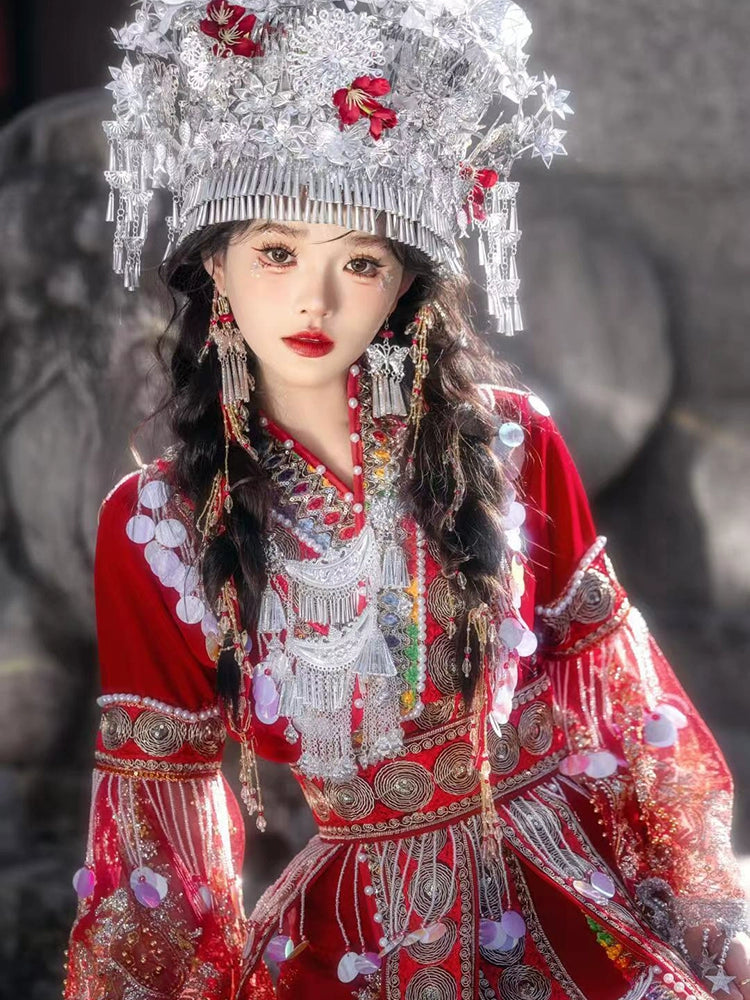 Close-up of embroidered red Miao performance dress with detailed silver jewelry and pearl accents, showcasing cultural craftsmanship.