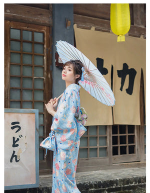 A woman in a light blue floral kimono yukata posing gracefully in front of a traditional Japanese backdrop. A stylish and elegant yukata dress.