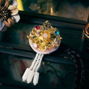 Pink Korean traditional headgear with gold floral and gemstone detailing, pearl tassels, and precise cutting craftsmanship.