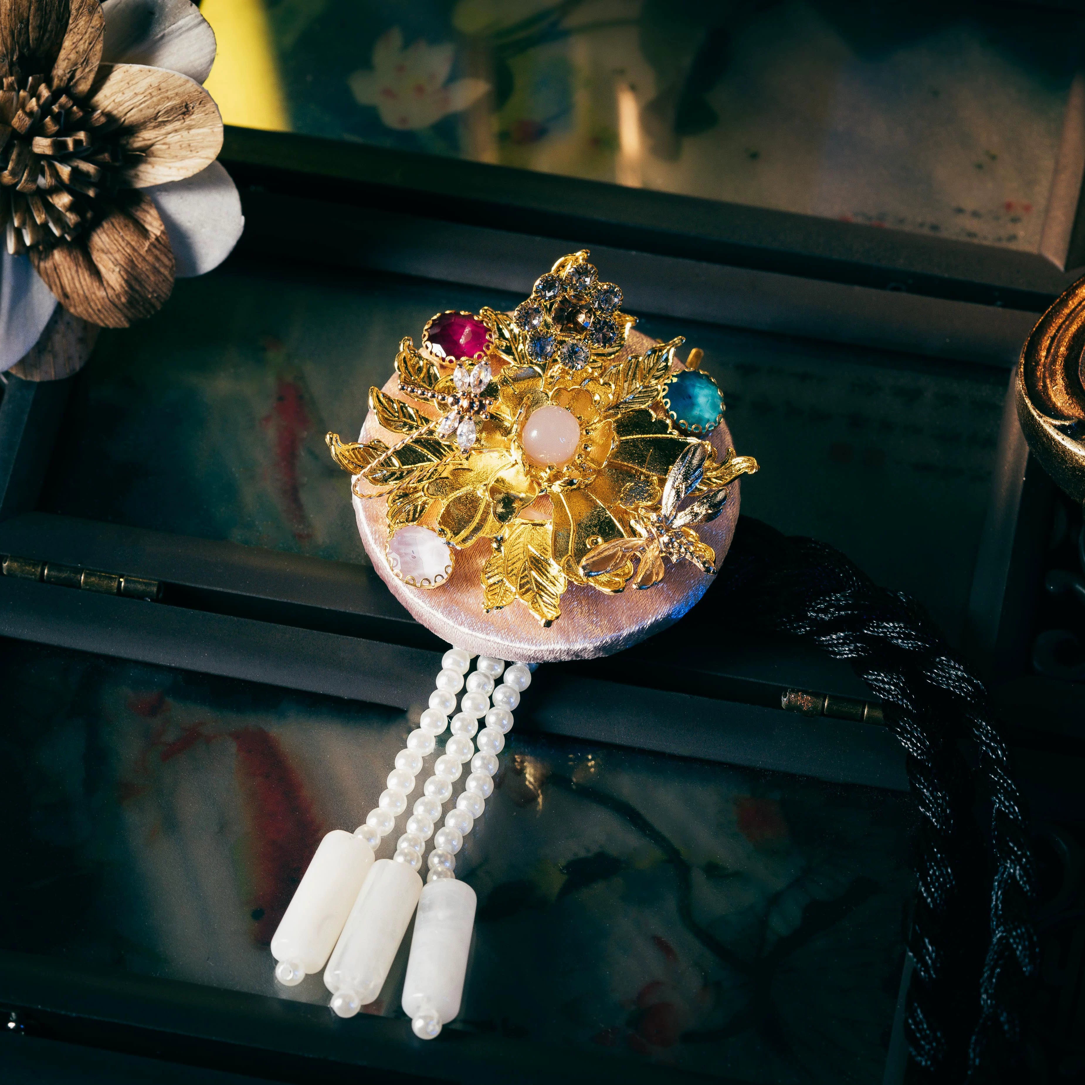 Pink Korean traditional headgear with gold floral and gemstone detailing, pearl tassels, and precise cutting craftsmanship.