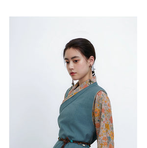 Side view of teal cross-collared Tibetan top with floral sleeves, model against white backdrop