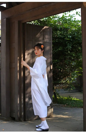 Woman in a white Yukata Kimono walking through a wooden gate, showcasing the dress's elegant drape and traditional Japanese aesthetic.