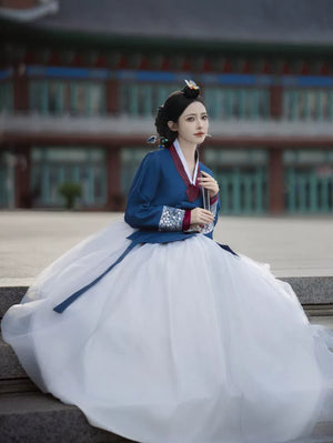 Woman in blue and white hanbok sitting on steps, traditional architecture backdrop - Yandan_Hanfu
