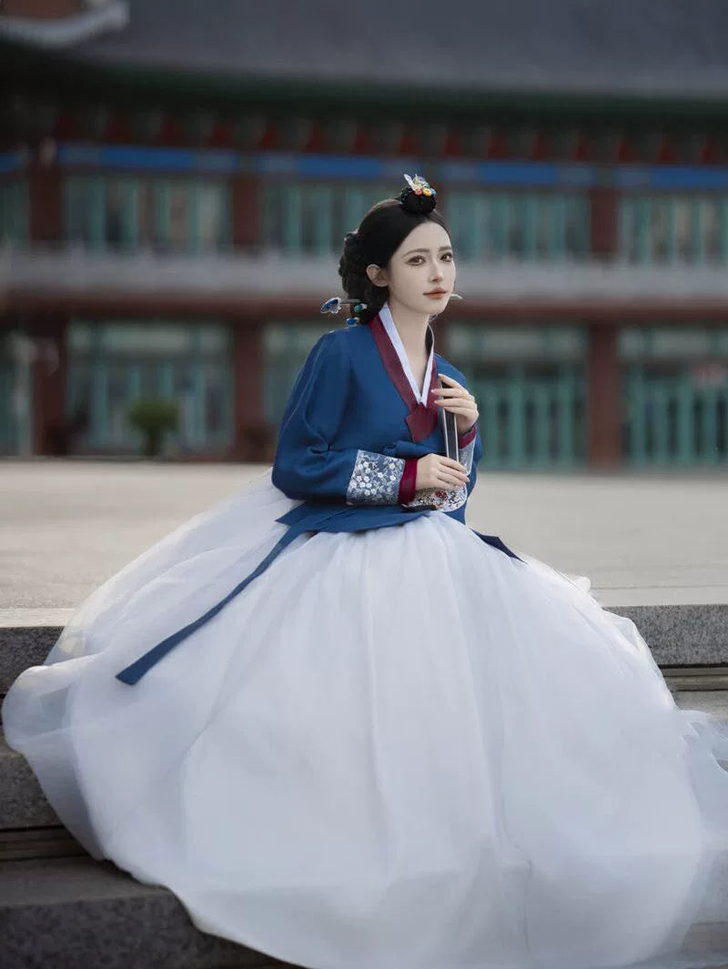 Woman in blue and white hanbok sitting on steps, traditional architecture backdrop - Yandan_Hanfu