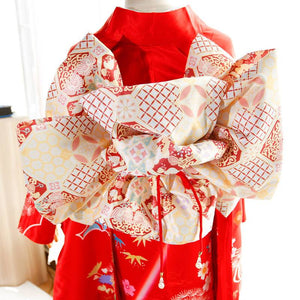 Close-up of cream and red big three-leaf bow belt on red kimono. Swinging sleeves and geisha-style design highlight traditional fashion.