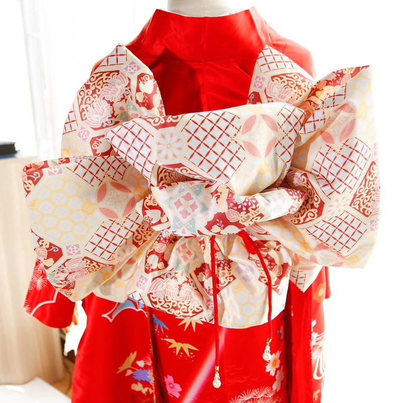Close-up of cream and red big three-leaf bow belt on red kimono. Swinging sleeves and geisha-style design highlight traditional fashion.