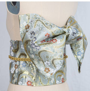 Light blue and gold brocade kimono waist seal with floral bow, ideal for yukata styling and enhancing traditional Japanese attire.