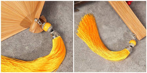 Close-up of yellow tassel and bamboo structure of folding fan. Elegant detail for Hanfu dance and traditional Chinese styling.