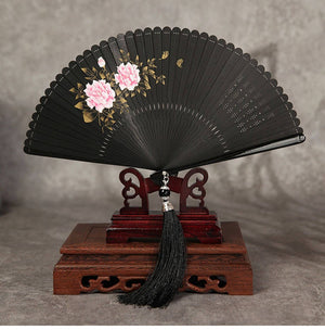 Black bamboo folding fan with pink peony flowers on wooden stand. Includes black tassel, ideal for Hanfu and traditional dance.