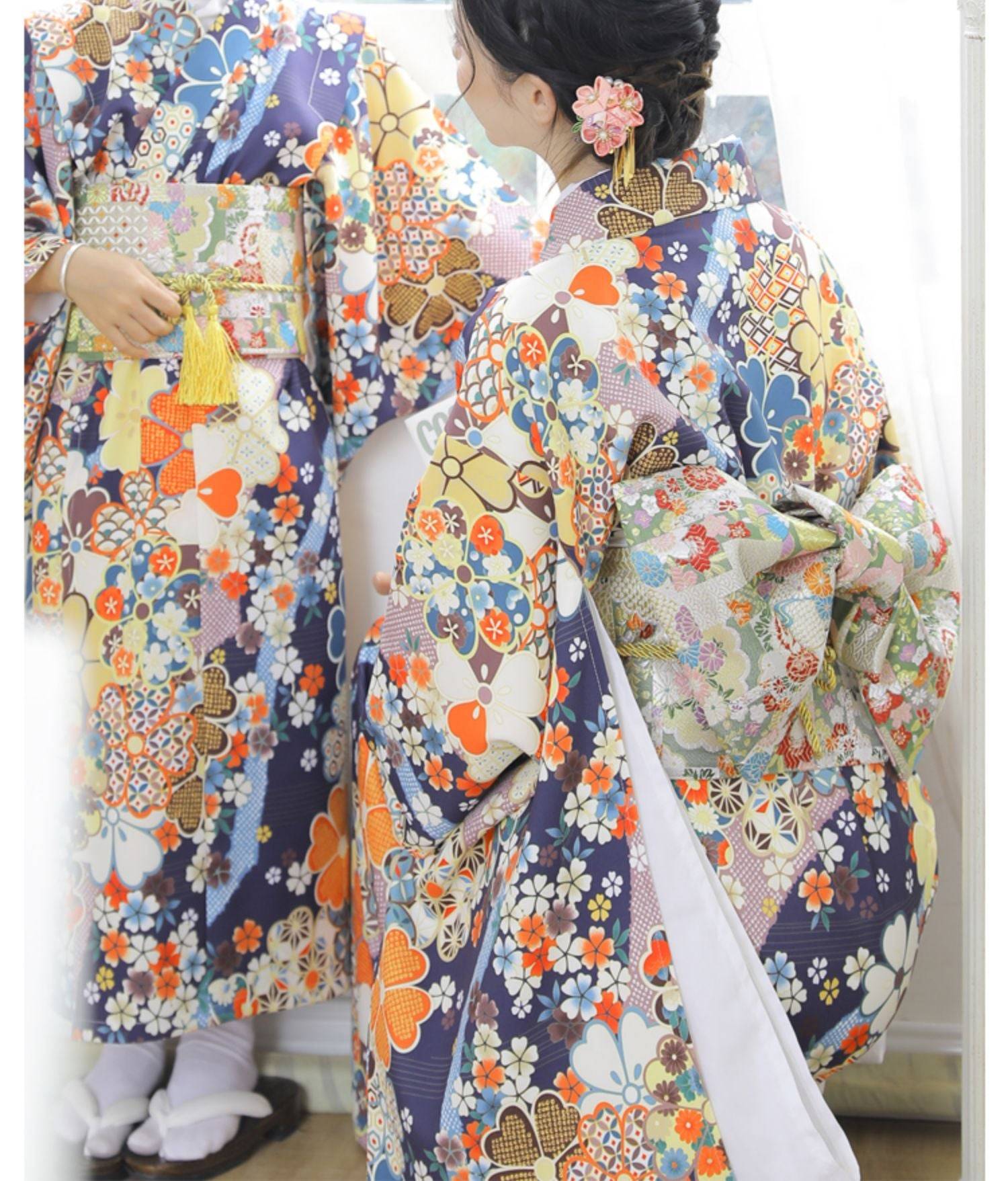 Women wearing colorful floral yukatas with brocade bow belts, showcasing traditional Japanese kimono waist styling for festive occasions.