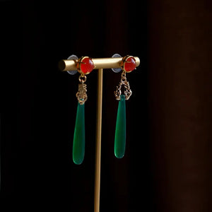 High-end green agate water drop earrings with red gemstone studs, displayed on a gold stand, ideal for traditional Chinese attire.