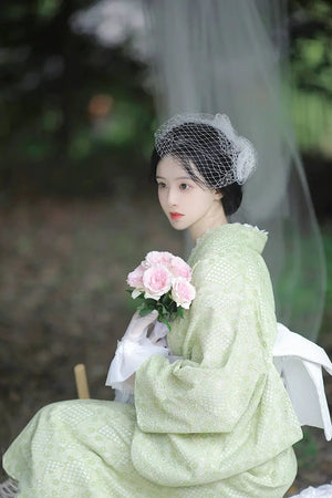 Model holding pink roses in a green kimono with white lace gloves.