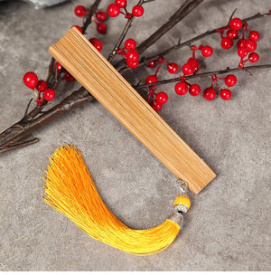 Closed natural bamboo fan with yellow tassel, laid flat near red berries. Lightweight and elegant for Hanfu dance.
