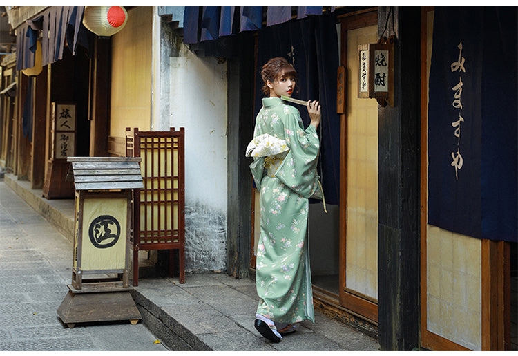 Woman in green floral yukata wearing a gold brocade bow belt, showcasing traditional Japanese kimono waist seal style.