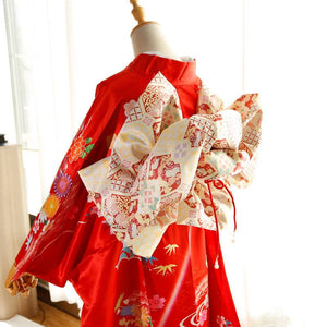 Side view of red kimono with cream patterned big three-leaf bow belt. Swinging sleeves and geisha-style belt bag complete the outfit.