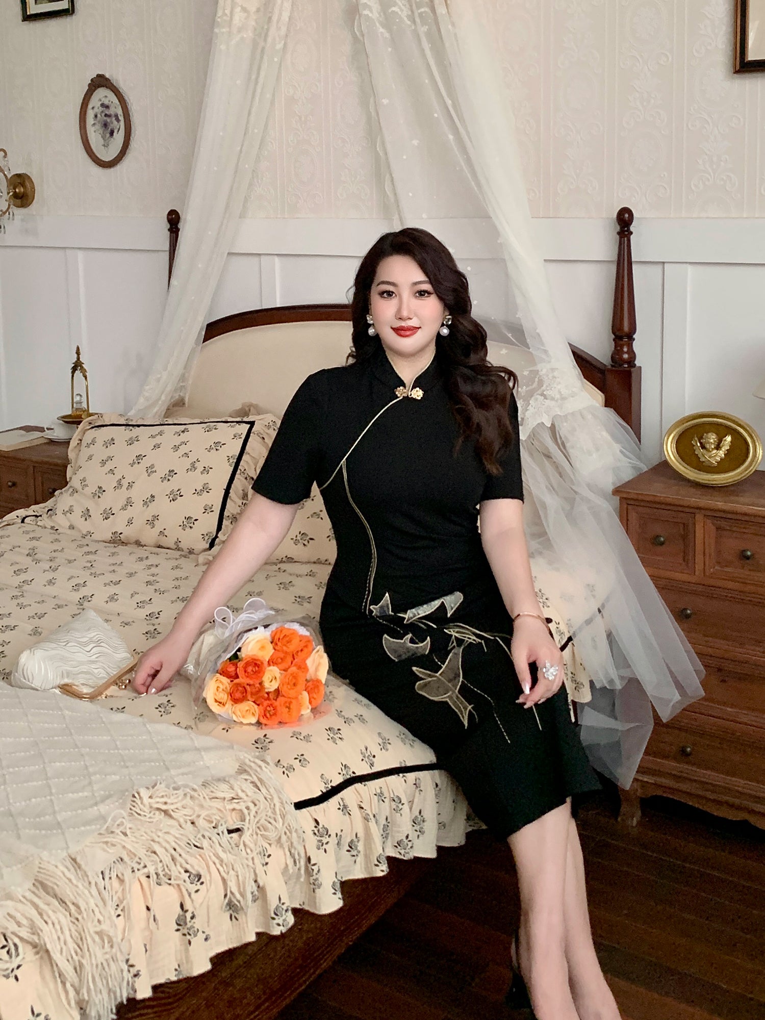Plus size black qipao dress with gold embroidery, styled with a bouquet of roses on a vintage bed for a romantic look.