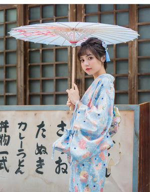 Side view of a woman wearing a light blue floral kimono yukata with a matching parasol. A charming and elegant Japanese-style dress.
