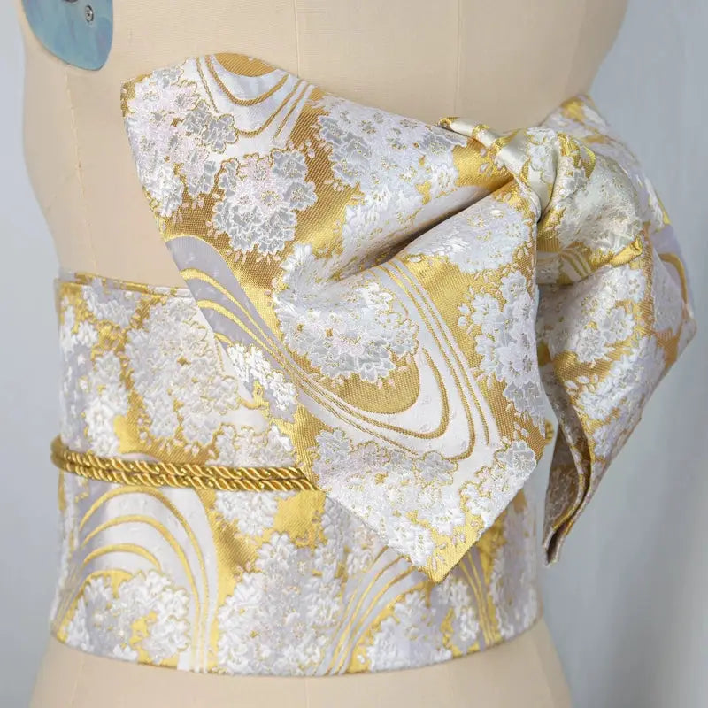 Gold and white brocade bow belt with floral patterns, styled on mannequin for Japanese kimono waist seal and yukata fashion shoots.