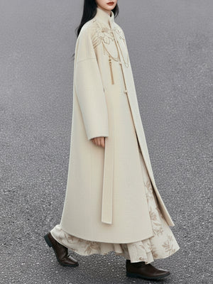 Person wearing a long, light-colored coat with floral patterns on a gray background