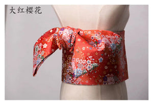 Yukata bow belt in vibrant red brocade with floral patterns, tied in an elegant styling knot. Perfect for enhancing traditional Japanese kimono outfits.