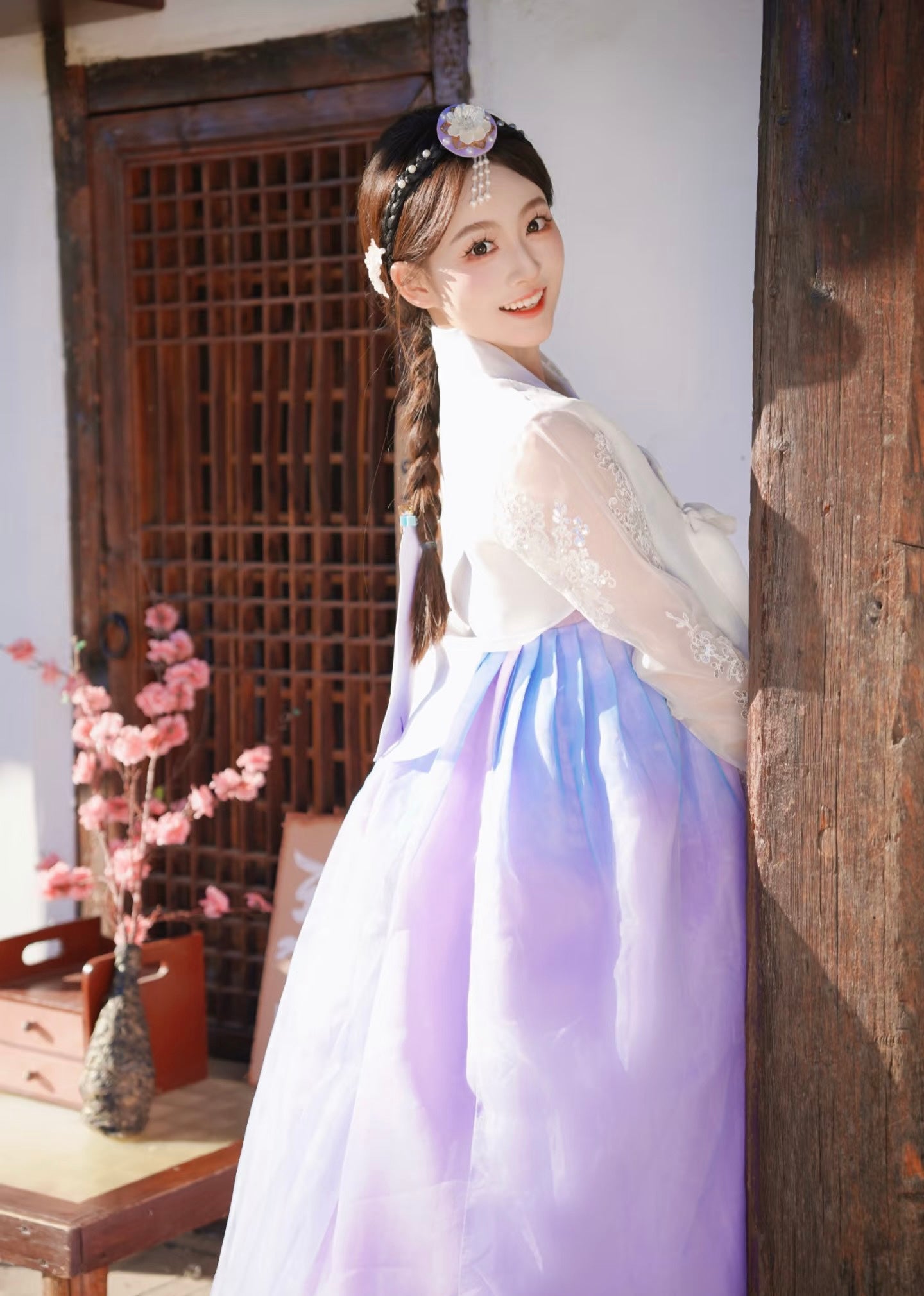 White purple Korean female high-end genuine Yanji court hanbok with sheer sleeves, smiling and posing near wooden pillar.