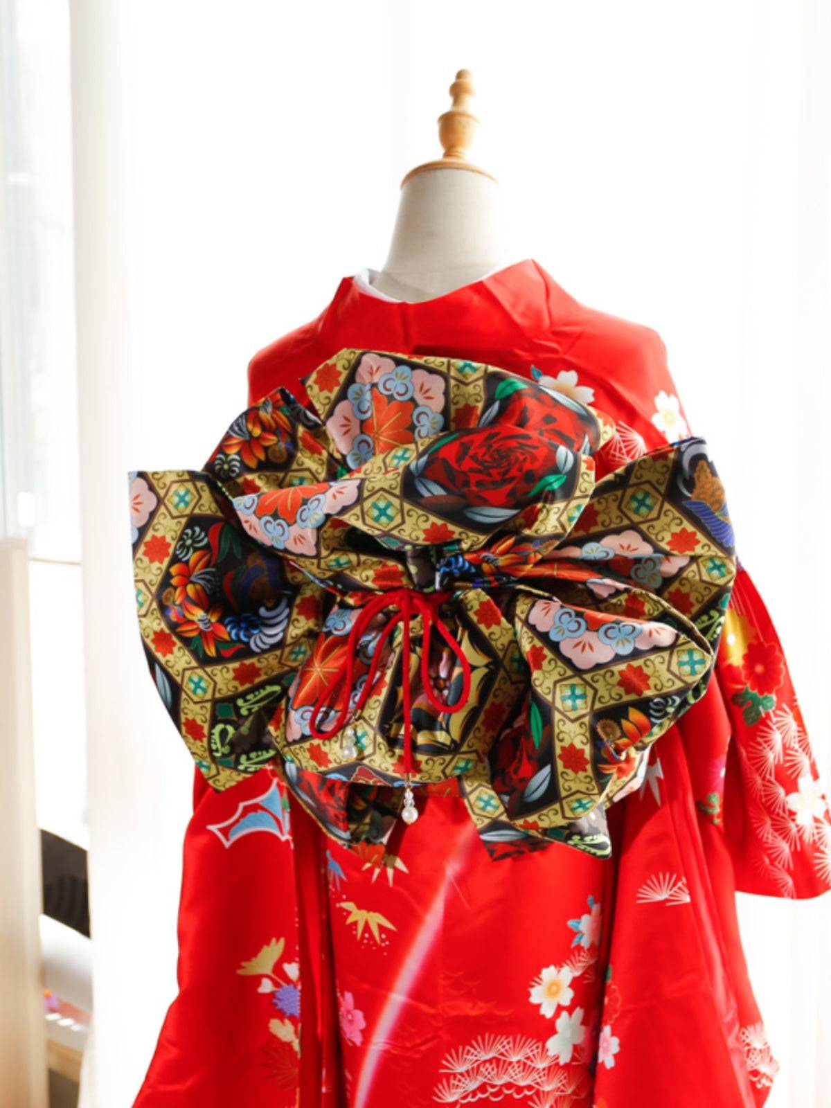 Red kimono with bold black and green floral big three-leaf bow belt. Traditional swinging sleeve kimono with vibrant geisha-inspired details.