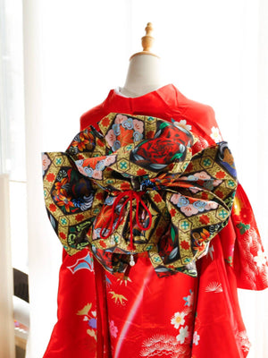 Red kimono with bold black and green floral big three-leaf bow belt. Traditional swinging sleeve kimono with vibrant geisha-inspired details.