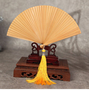 Natural bamboo folding fan with yellow tassel on wooden stand. Ideal for traditional Chinese performances and Hanfu styling.