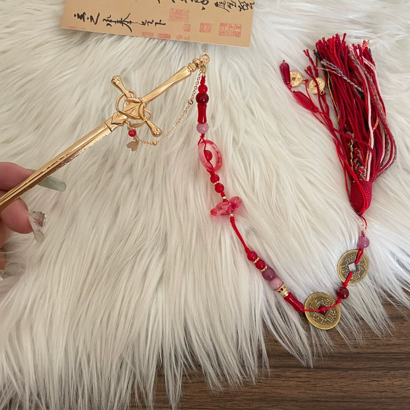 Chinese sword tassel hairpin with red string, gold coins, and ornate sword pin, displayed on white fur for product showcase.