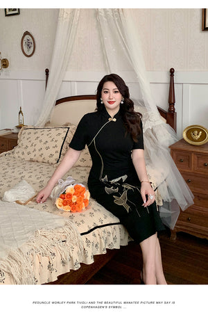 Elegant black plus size cheongsam dress with gold bird embroidery, styled in a cozy vintage bedroom with floral accents.
