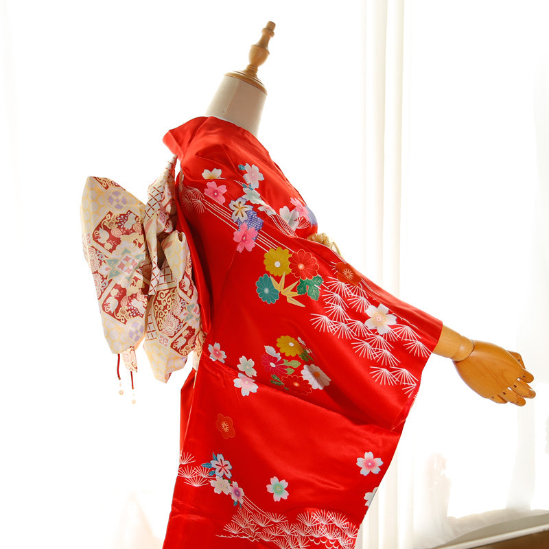Side view of red kimono with floral patterns and cream big three-leaf bow belt. Swinging sleeves and geisha-style belt included.