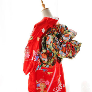 Side view of red kimono with swinging sleeves and bold floral big three-leaf bow belt. Geisha-inspired belt enhances traditional appeal.