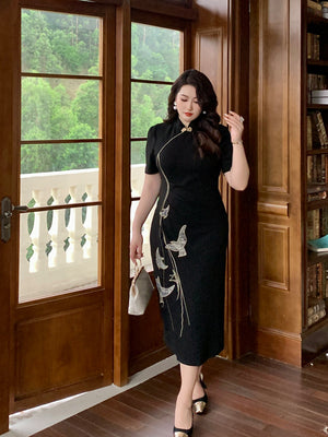 Black embroidered plus size cheongsam dress featuring gold bird motifs, worn in a luxurious interior with scenic balcony view.