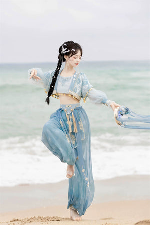 Model in motion wearing blue Hanfu Princess Jasmine suit by 【Cloud Traveler】, styled with gold tassels and beach scenery.