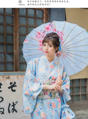 Close-up of a woman in a light blue floral kimono yukata holding a matching parasol. A soft and elegant Japanese-inspired dress with a delicate touch.