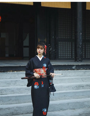 Close-up of a woman in a black yukata holding a fox mask, showcasing red and blue floral patterns. Perfect for Halloween or literary events.