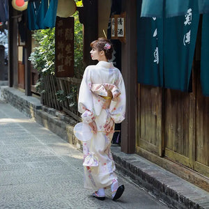 Back view of a women's Japanese kimono dress in soft beige with floral prints. Features a decorative obi bow for a refined yukata look.