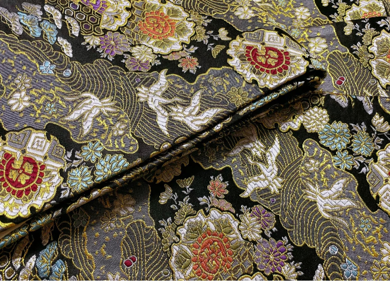 Close-up of black brocade fabric with gold and red floral motifs, used in Japanese kimono waist seal and yukata belts.