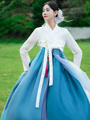 Blue hanbok princess dress with white top and decorative tassels, grassy outdoor setting