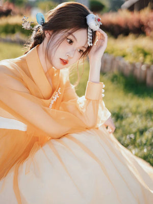 Serene woman in an orange Yanbian Yanji Korean Hanbok dress, resting on the grass with intricate hair accessories, exuding traditional elegance.