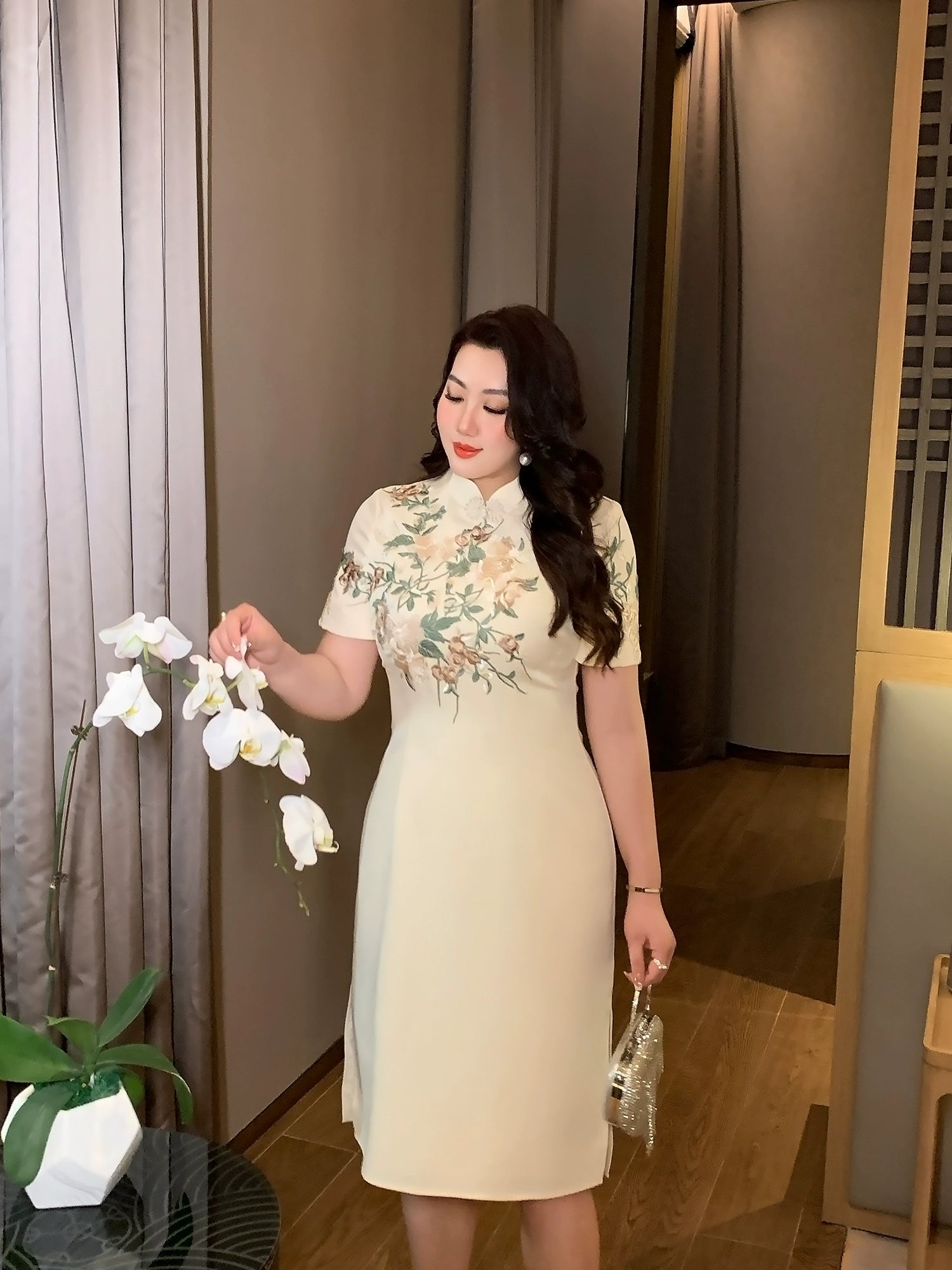 Champagne plus size cheongsam/qipao with floral embroidery, styled with a clutch for a refined evening look.