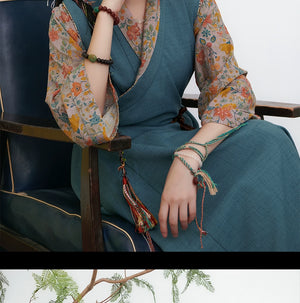 Close-up of teal Tibetan dress with floral sleeves, model sitting with decorative tassels and bracelets