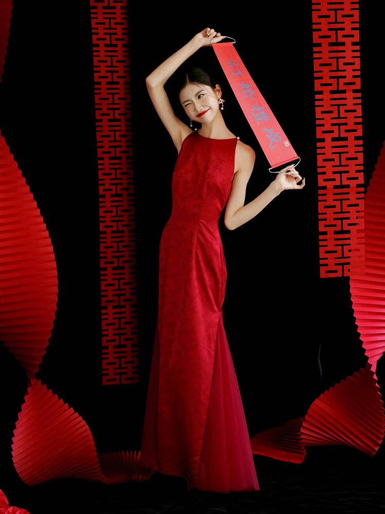 Bride in red yarn cheongsam dress with fan, standing in soft-lit setting, ideal for wedding or engagement.