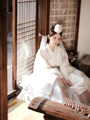 White Yanji Hanbok court dress with floral embroidery, worn indoors with traditional decor, perfect for Korean cultural fashion.