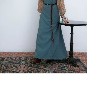 Tibetan-inspired long teal skirt with braided belt, standing near table