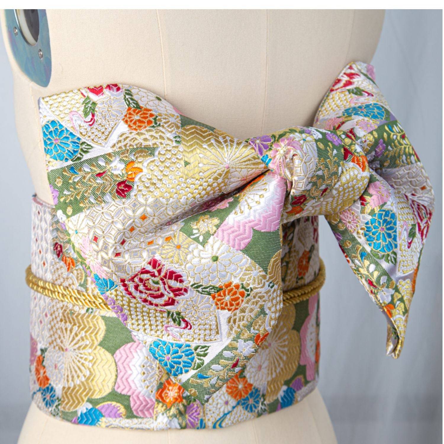 Colorful floral brocade bow belt for yukata, styled on mannequin for traditional Japanese kimono waist seal and fashion photography.