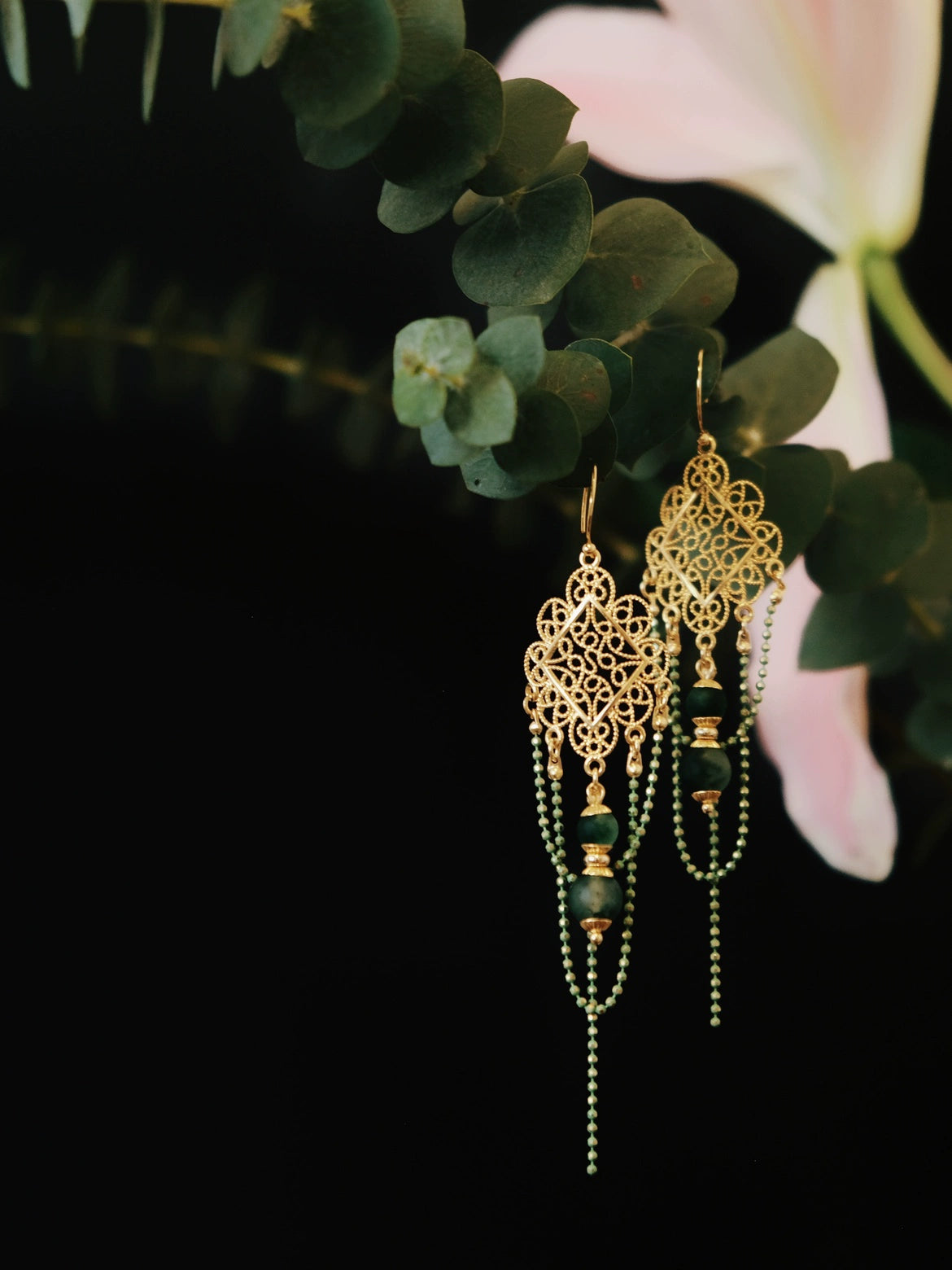Su Mask Ear Clips - Hanfu Gold Tassel Earrings with green beads and floral filigree, hanging on eucalyptus with soft pink lily accent.