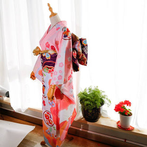 Front angle of pink kimono with floral prints and purple big three-leaf bow belt. Swinging sleeves and geisha-style belt complete the look.
