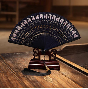 Blue bamboo fan with floral cutouts on wooden stand, black tassel. Elegant Hanfu accessory for traditional Chinese performances.